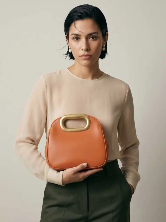Model holding an orange top-handle bag